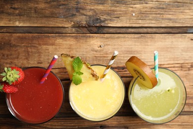 Delicious colorful juices in glasses on wooden table, flat lay. Space for text