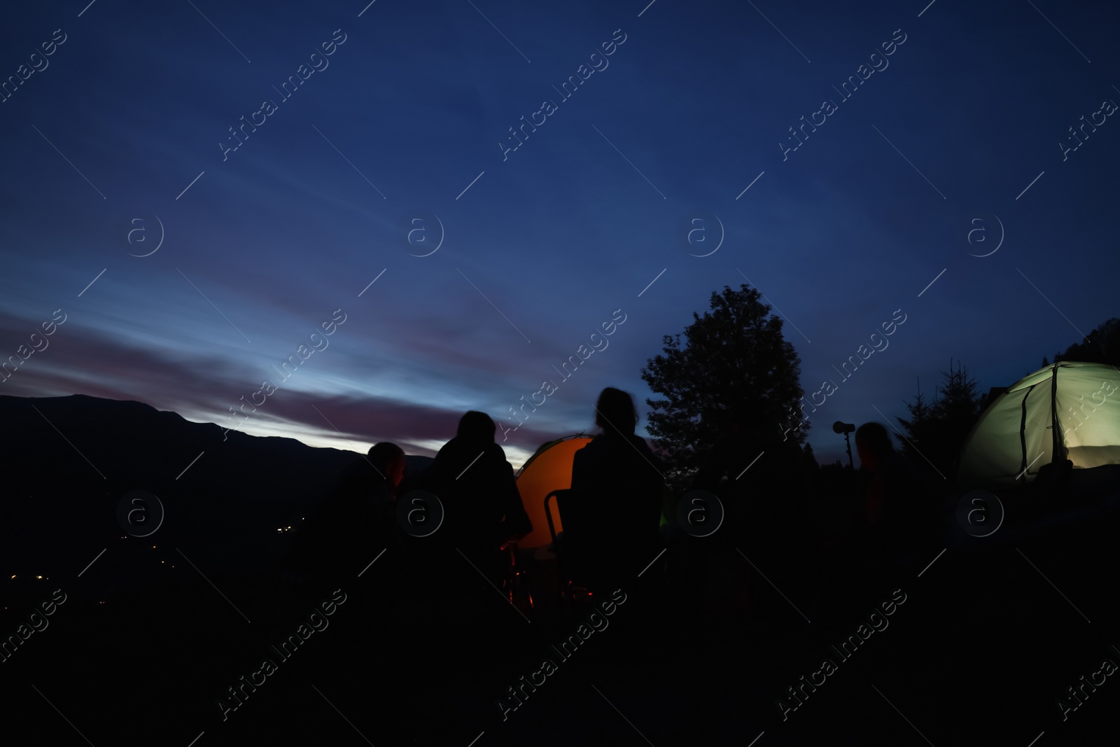 Photo of Group of friends near camping tents outdoors in evening