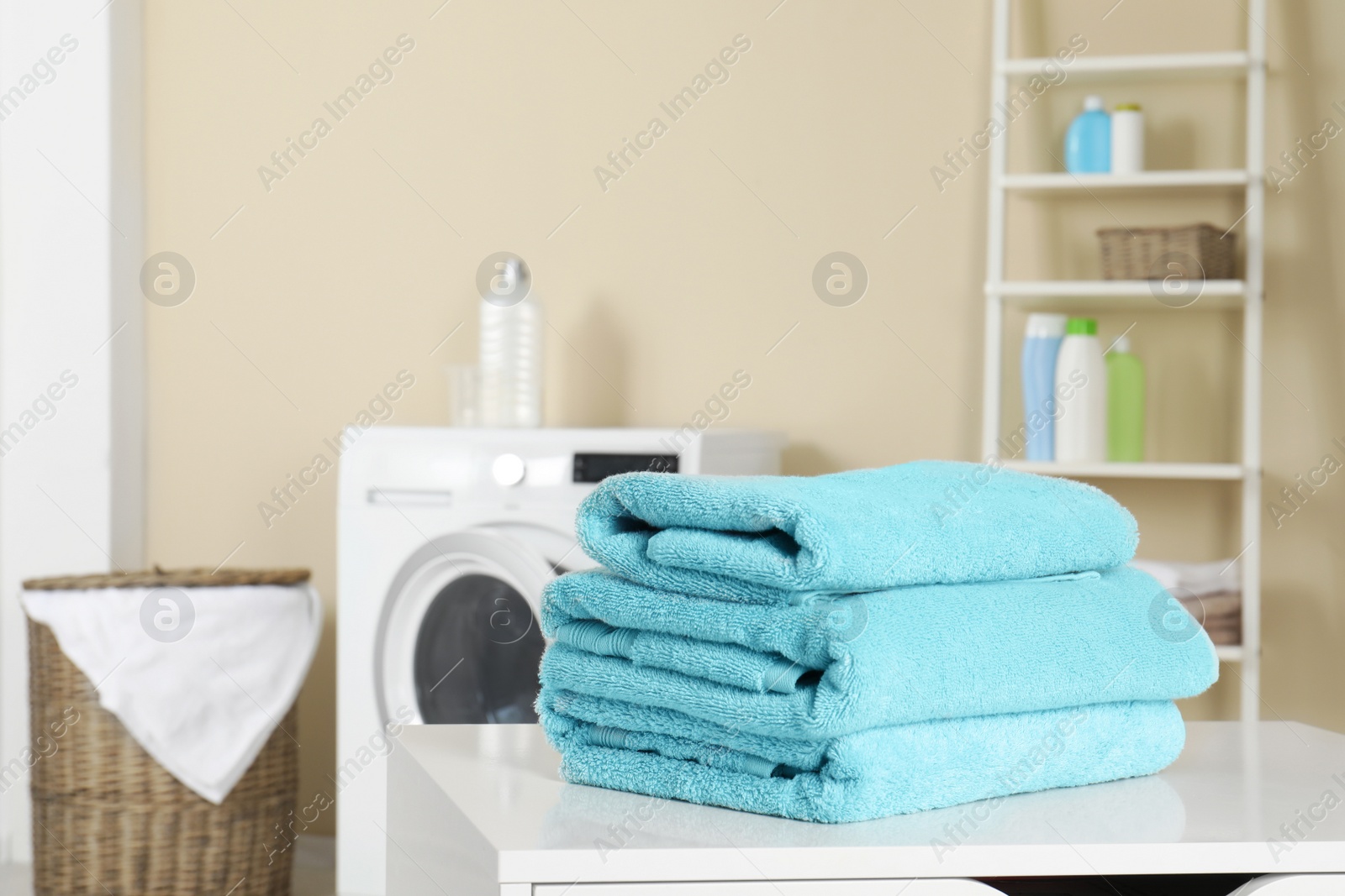Photo of Stack of clean soft towels on table in laundry room. Space for text