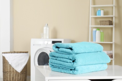 Stack of clean soft towels on table in laundry room. Space for text