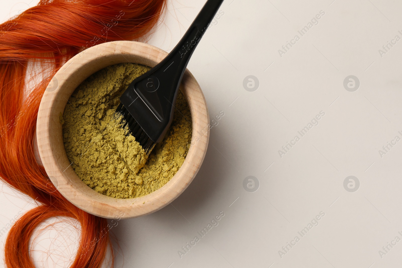 Photo of Henna powder, brush and red strand on white table, flat lay with space for text. Natural hair coloring