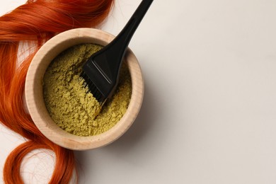 Photo of Henna powder, brush and red strand on white table, flat lay with space for text. Natural hair coloring