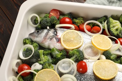 Raw fish with vegetables and lemon in baking dish on table