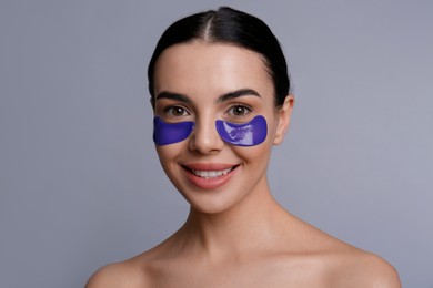 Beautiful young woman with under eye patches on grey background