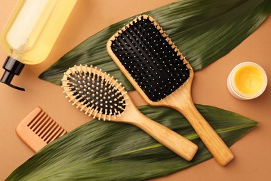 Photo of Flat lay composition with wooden hairbrushes and cosmetic products on light brown background