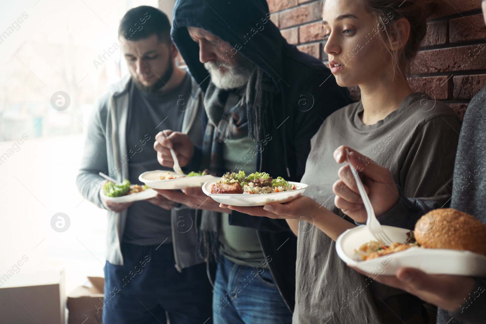 Photo of Poor people with plates of food at wall indoors