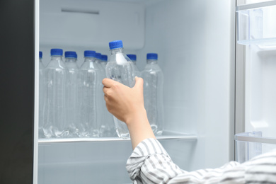Woman taking bottle of water from refrigerator, closeup