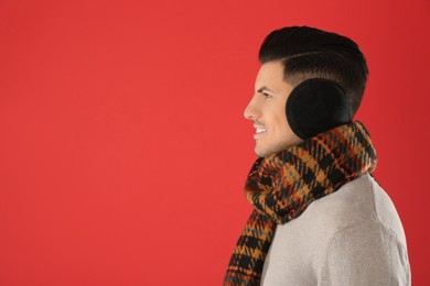 Photo of Man wearing stylish earmuffs and scarf on red background. Space for text