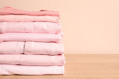 Photo of Stack of baby girl's clothes on wooden table. Space for text