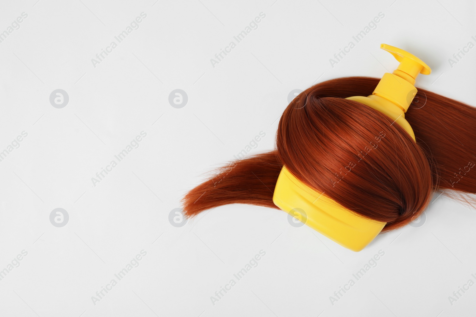 Photo of Shampoo bottle wrapped in lock of hair isolated on white, top view. Natural cosmetic products