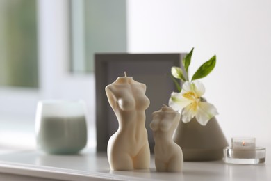Photo of Beautiful body shaped candles and flower on white table indoors