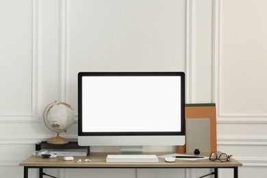 Stylish workspace with computer and stationery on wooden desk near white wall