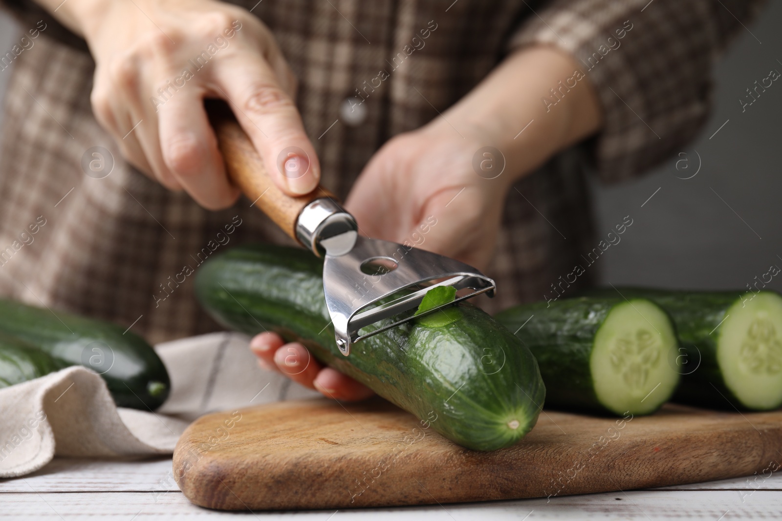 Photo of Woman peeling fresh cucumber at white wooden table, closeup