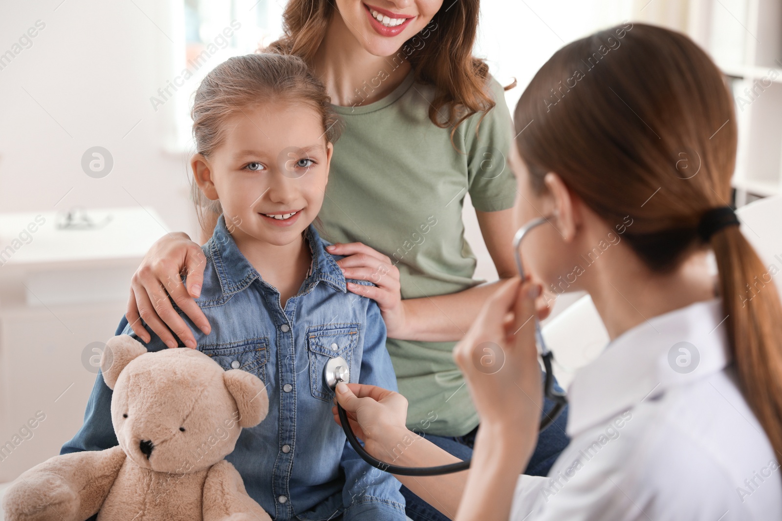 Photo of Mother and daughter visiting pediatrician. Doctor examining little patient with stethoscope in hospital