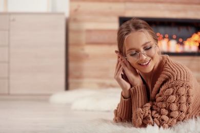 Photo of Beautiful young woman on rug at home, space for text. Winter atmosphere