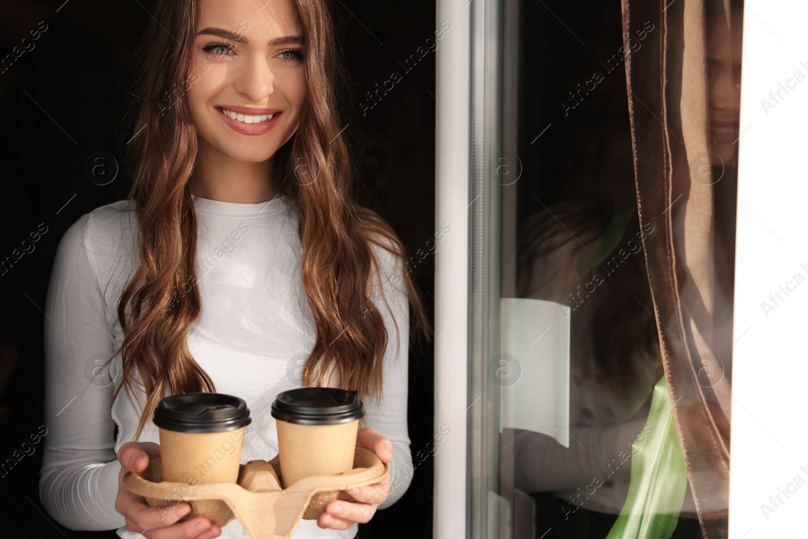 Photo of Happy young woman holding paper coffee cups indoors