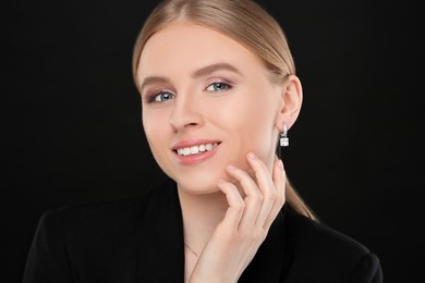 Beautiful young woman with elegant earrings on black background