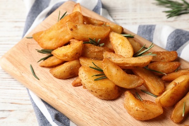 Photo of Wooden board with baked potatoes and rosemary on table, closeup