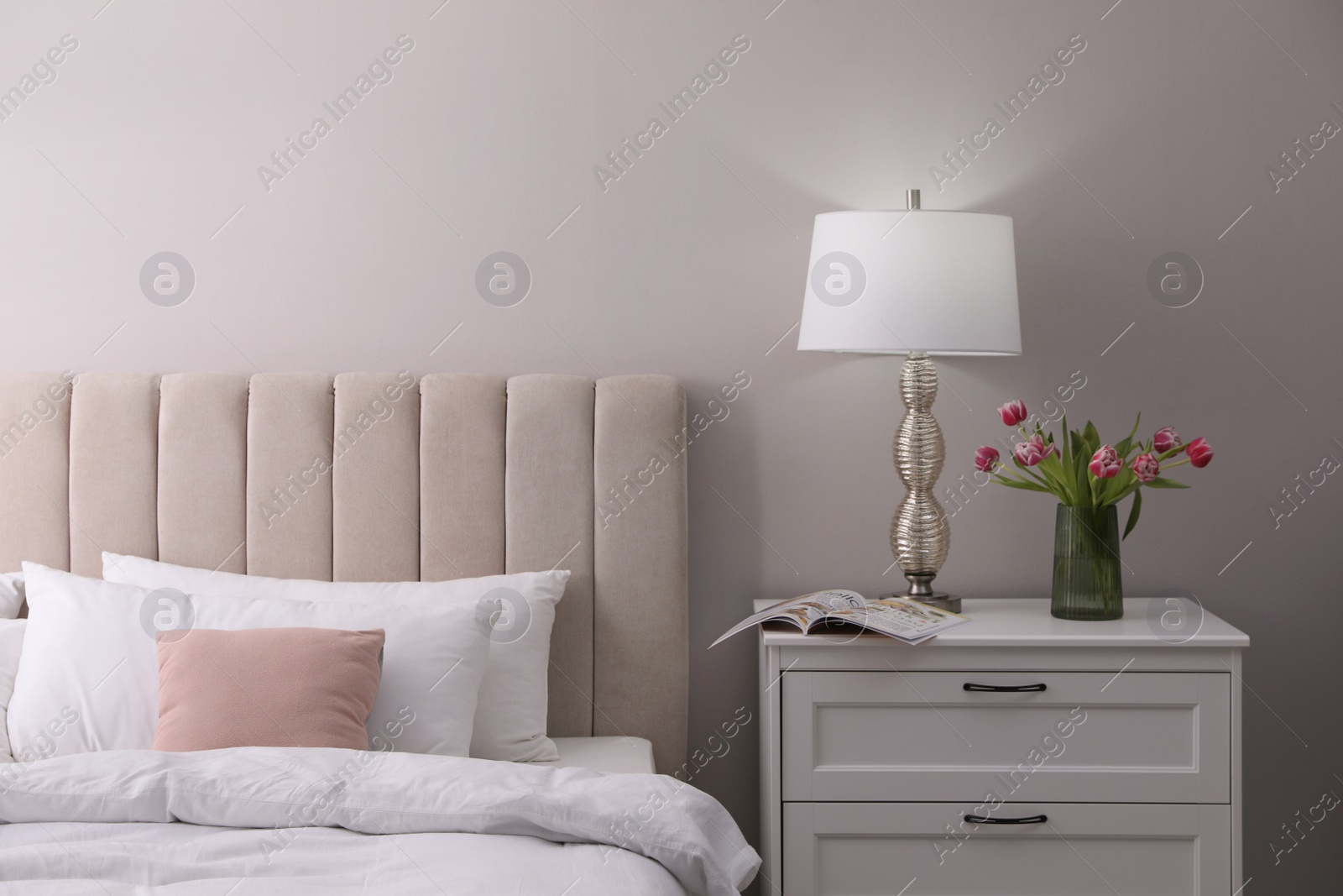 Photo of Stylish lamp, flowers and magazine on bedside table indoors. Bedroom interior elements