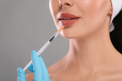 Doctor giving lips injection to young woman on light grey background, closeup. Cosmetic surgery