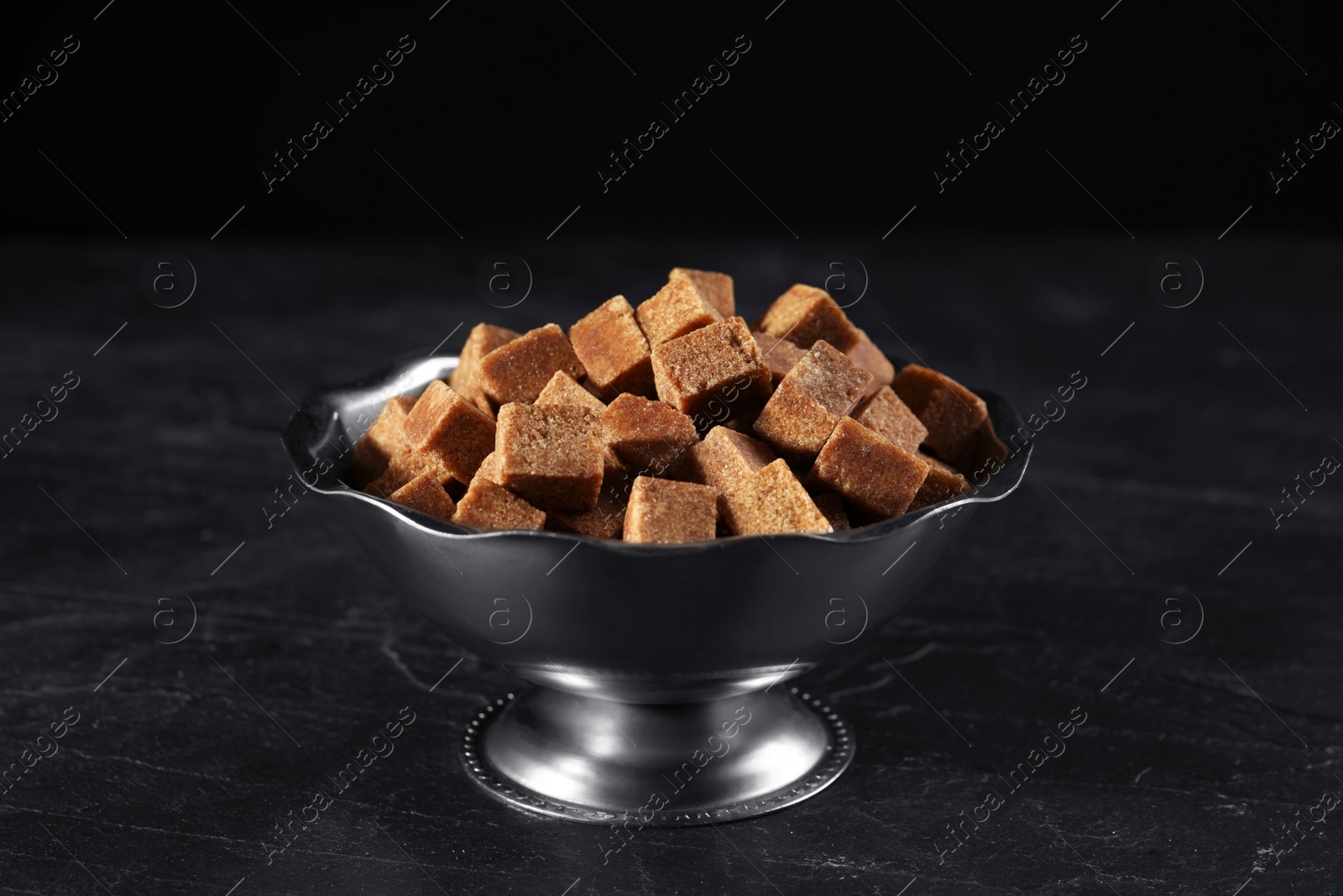 Photo of Metal bowl with brown sugar cubes on black table