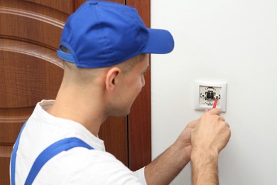Photo of Professional electrician with screwdriver repairing light switch indoors, focus on hands