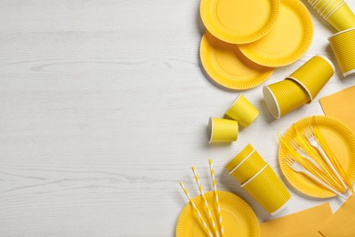Photo of Yellow disposable tableware on white wooden background, flat lay. Space for text