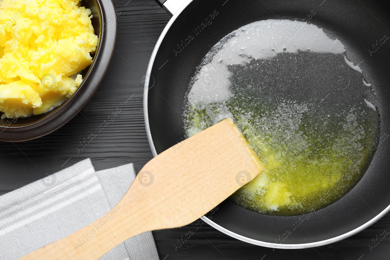 Photo of Frying pan and bowl with Ghee butter on dark wooden table, flat lay