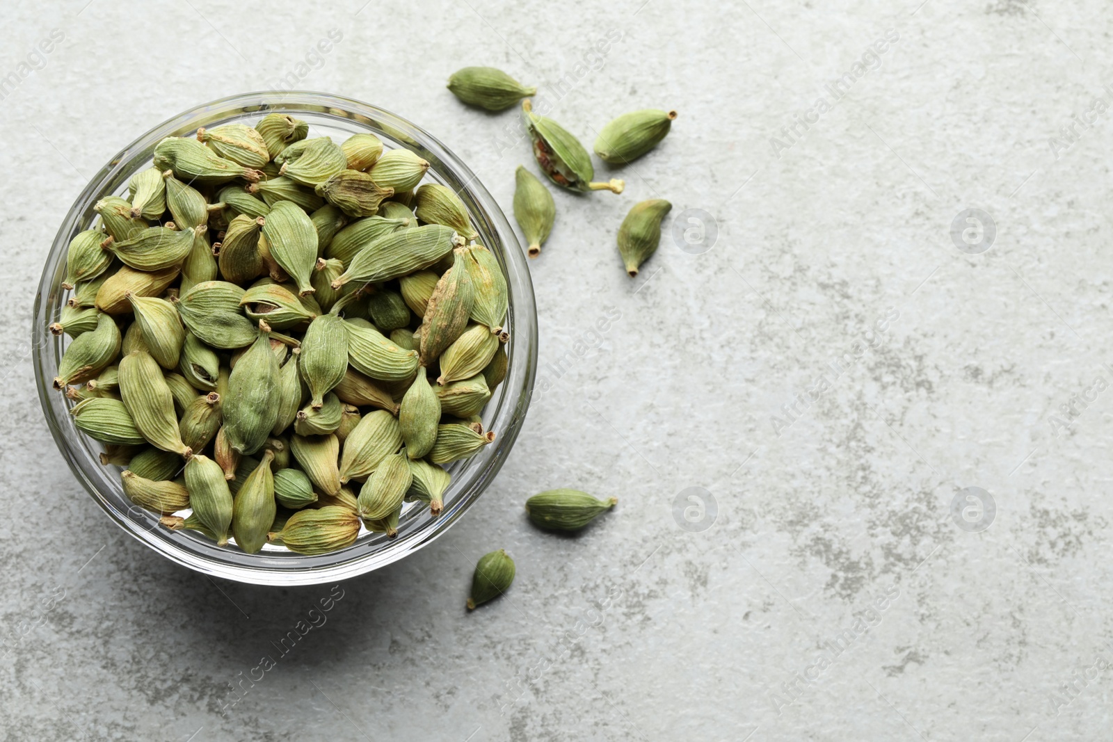 Photo of Glass bowl of dry cardamom pods on light grey table, top view. Space for text