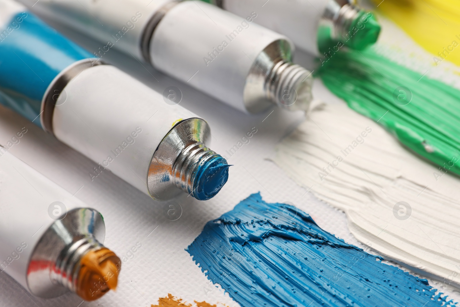 Photo of Tubes with oil paints and strokes on white canvas, closeup