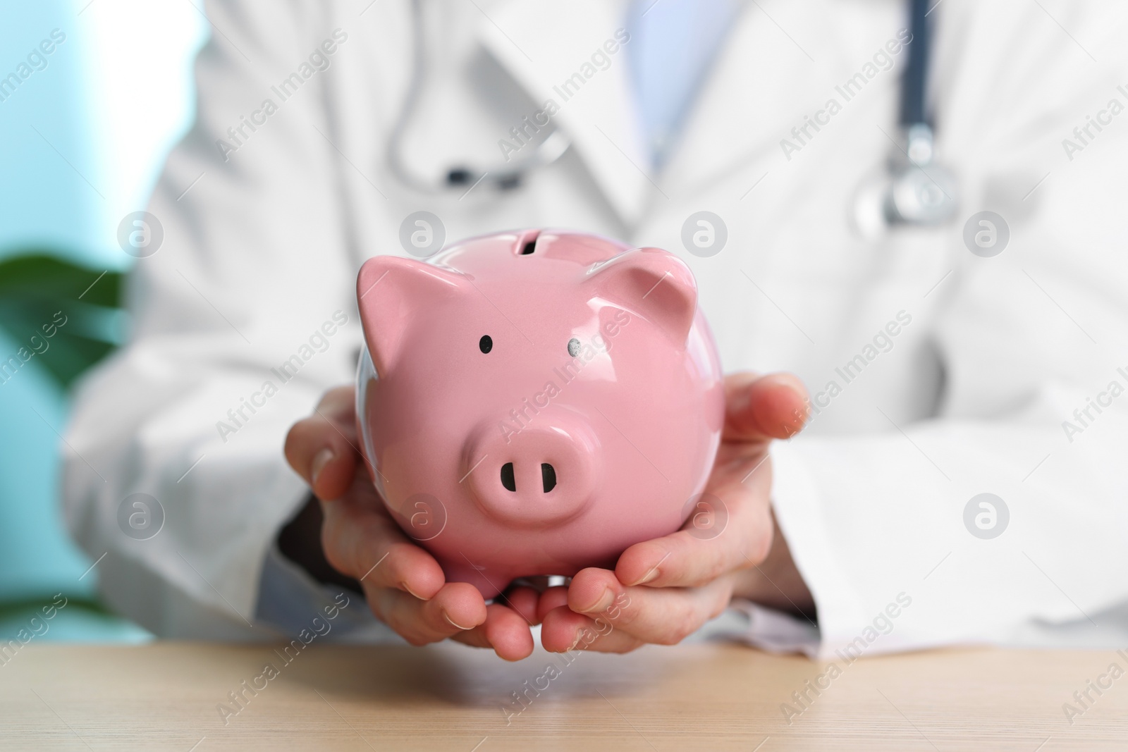 Photo of Doctor with piggy bank at wooden table, closeup