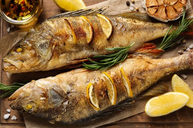 Photo of Tasty homemade roasted perches with rosemary and lemon on wooden board, flat lay. River fish