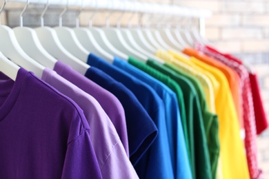 Rack with rainbow clothes on brick wall background