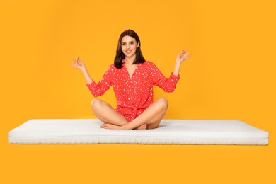 Photo of Young woman meditating on soft mattress against orange background