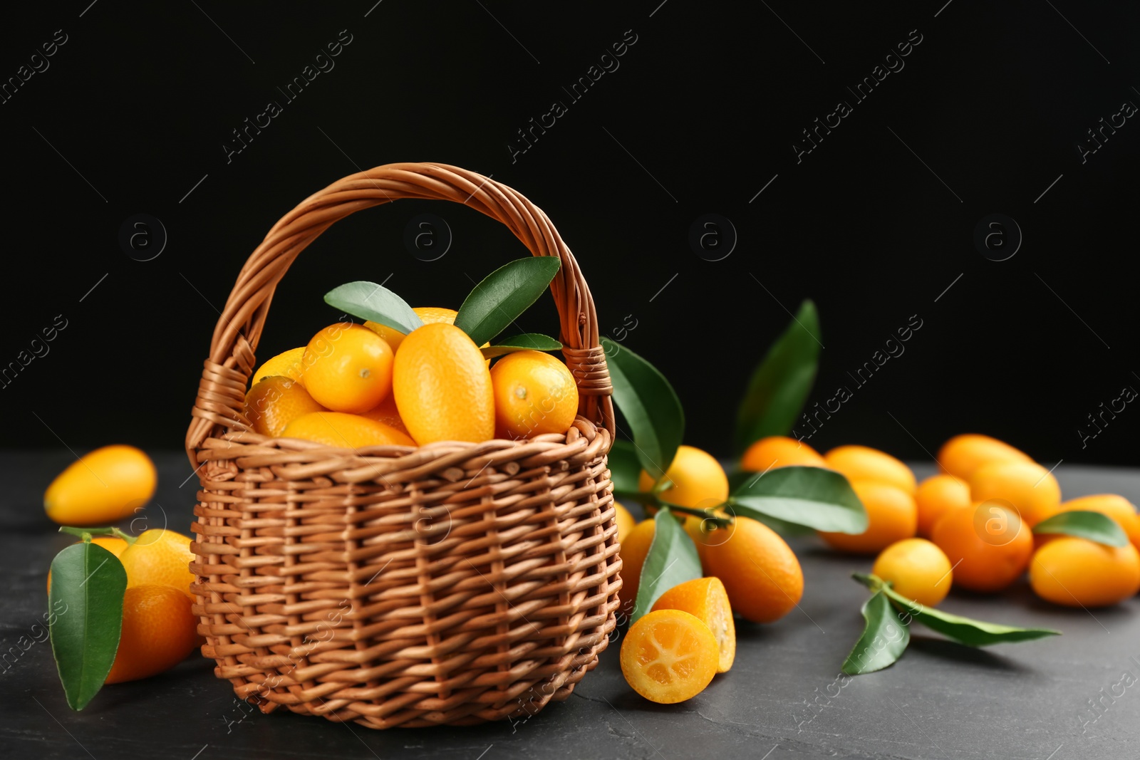 Photo of Fresh ripe kumquats in wicker basket on black table, space for text