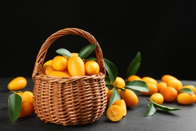 Photo of Fresh ripe kumquats in wicker basket on black table, space for text