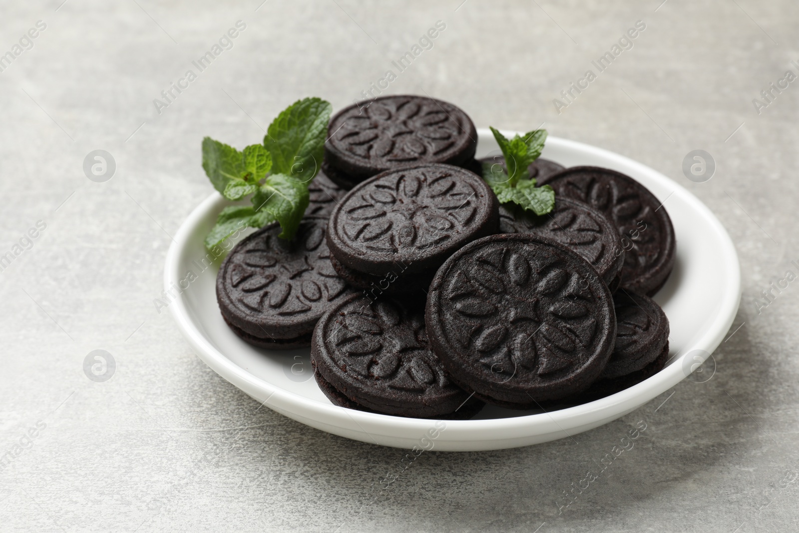 Photo of Plate with tasty sandwich cookies and mint on grey textured table, closeup