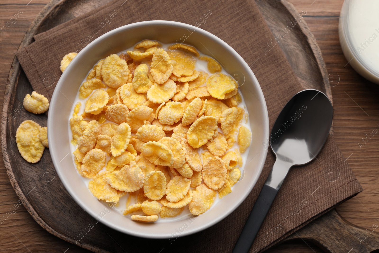 Photo of Tasty cornflakes with milk in bowl served on wooden table, flat lay