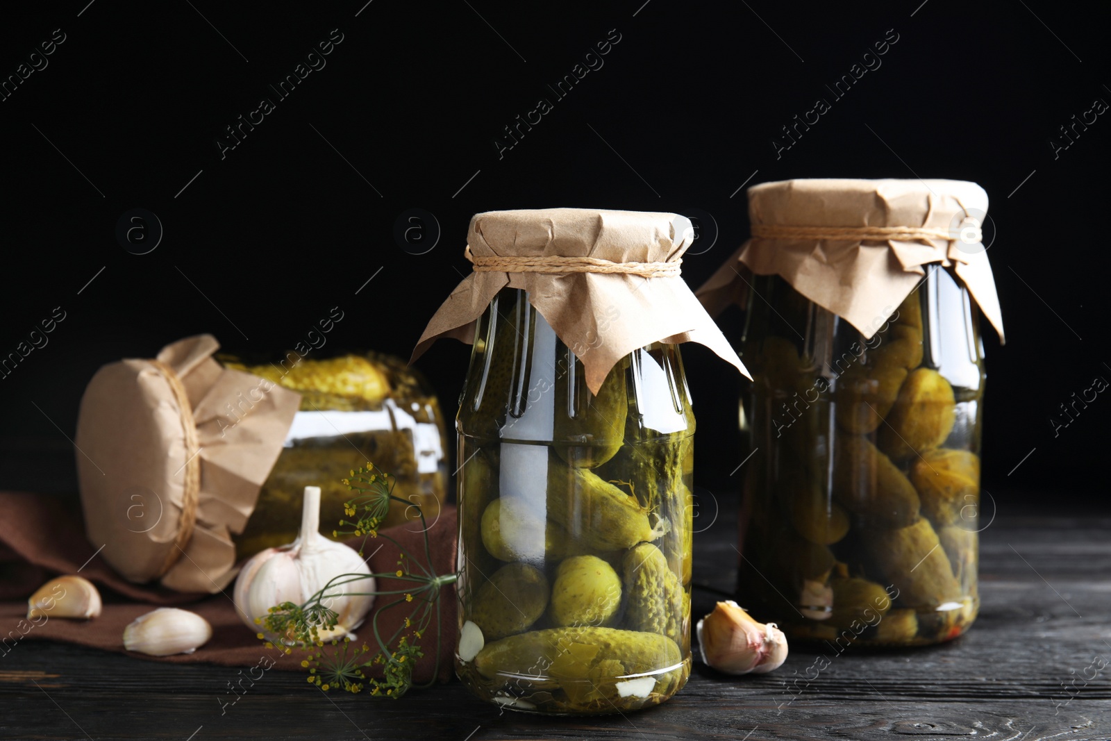 Photo of Jars with pickled cucumbers on wooden table against black background