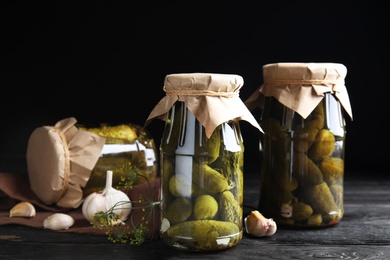 Photo of Jars with pickled cucumbers on wooden table against black background