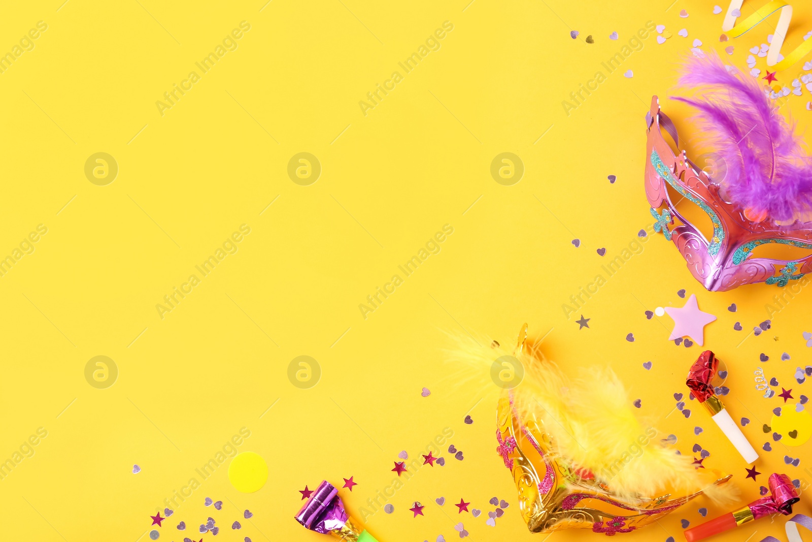 Photo of Beautiful carnival masks and party decor on yellow background, flat lay. Space for text