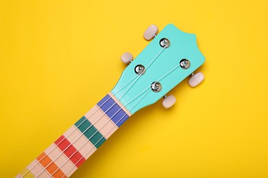 Photo of Head stock of colorful ukulele on yellow background, top view. String musical instrument