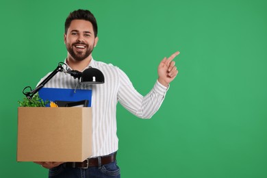 Happy unemployed man with box of personal office belongings on green background. Space for text