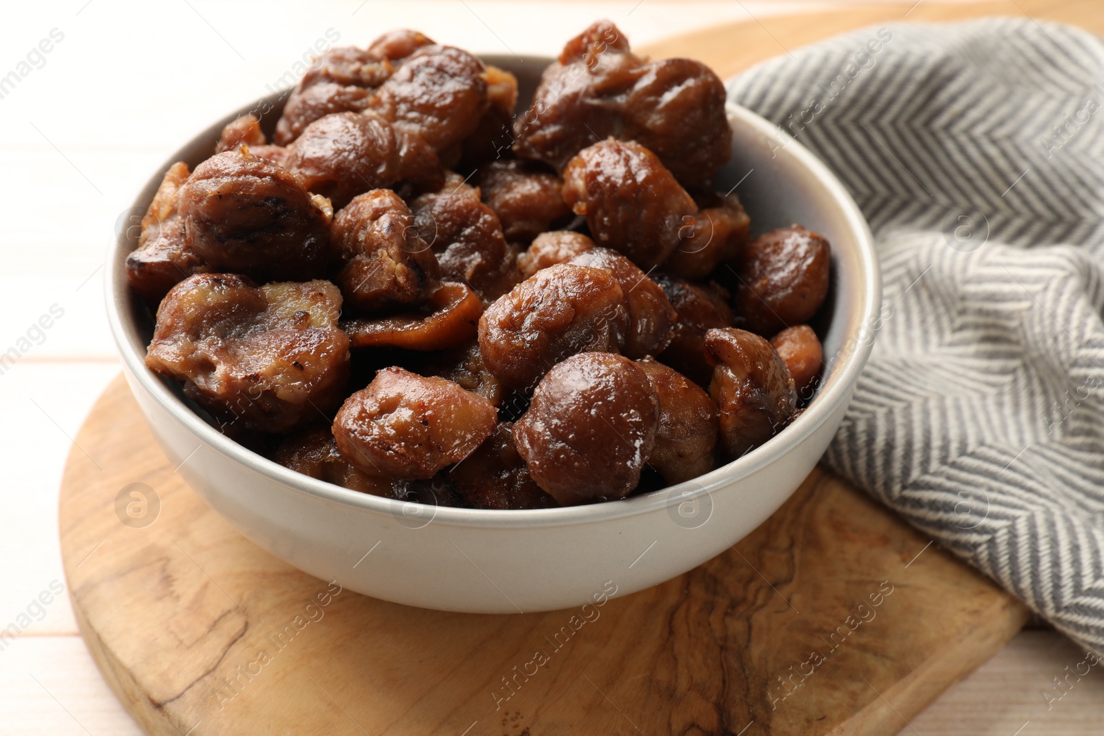 Photo of Roasted edible sweet chestnuts in bowl on table, closeup