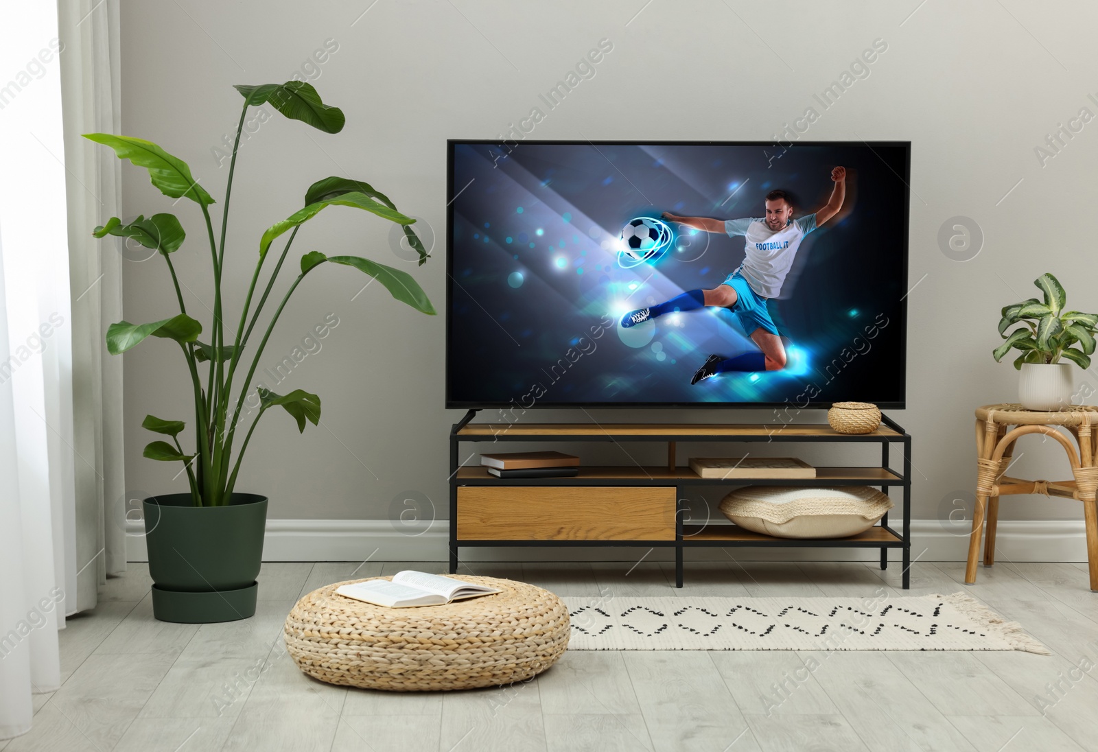 Image of Modern TV set on wooden stand in room. Scene of football broadcasting