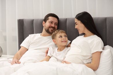 Happy pregnant woman with her son and husband in bed at home