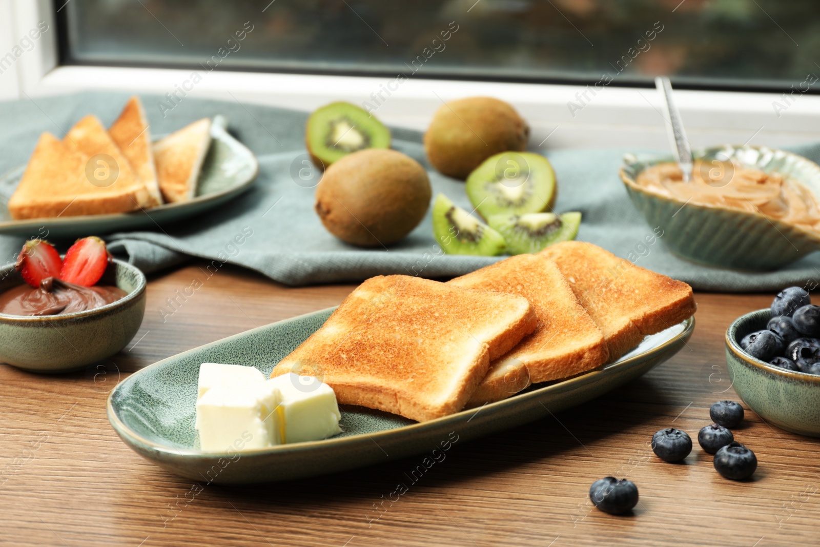 Photo of Tasty toasts and different toppings on wooden table at window