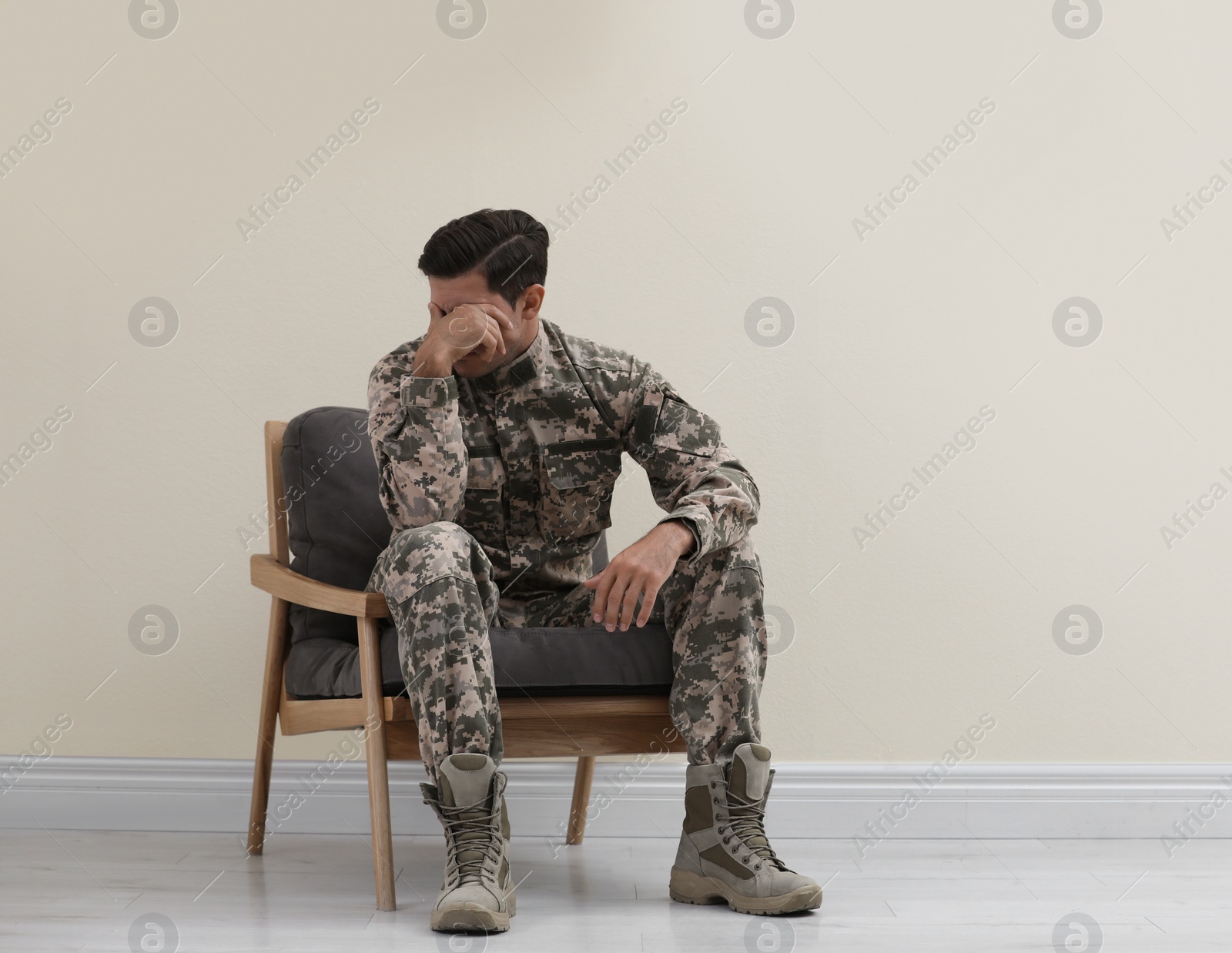 Photo of Stressed military officer sitting in armchair near white wall indoors. Space for text