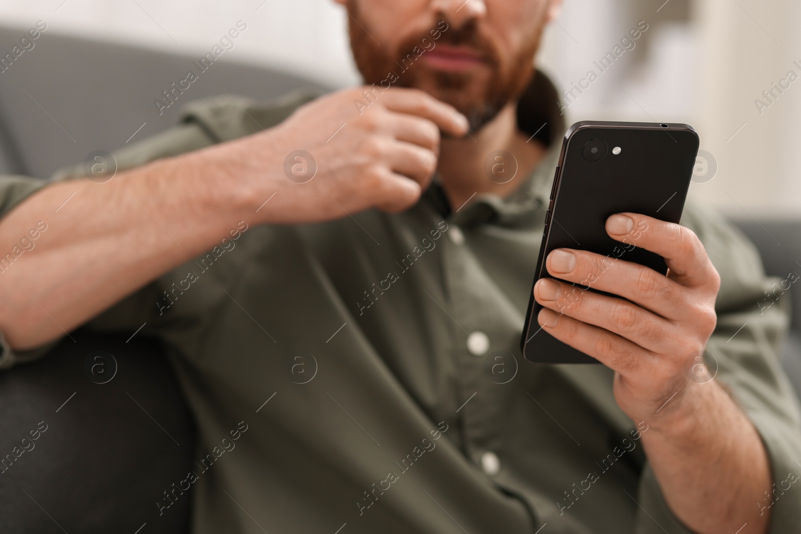 Photo of Handsome man using smartphone on sofa at home, closeup