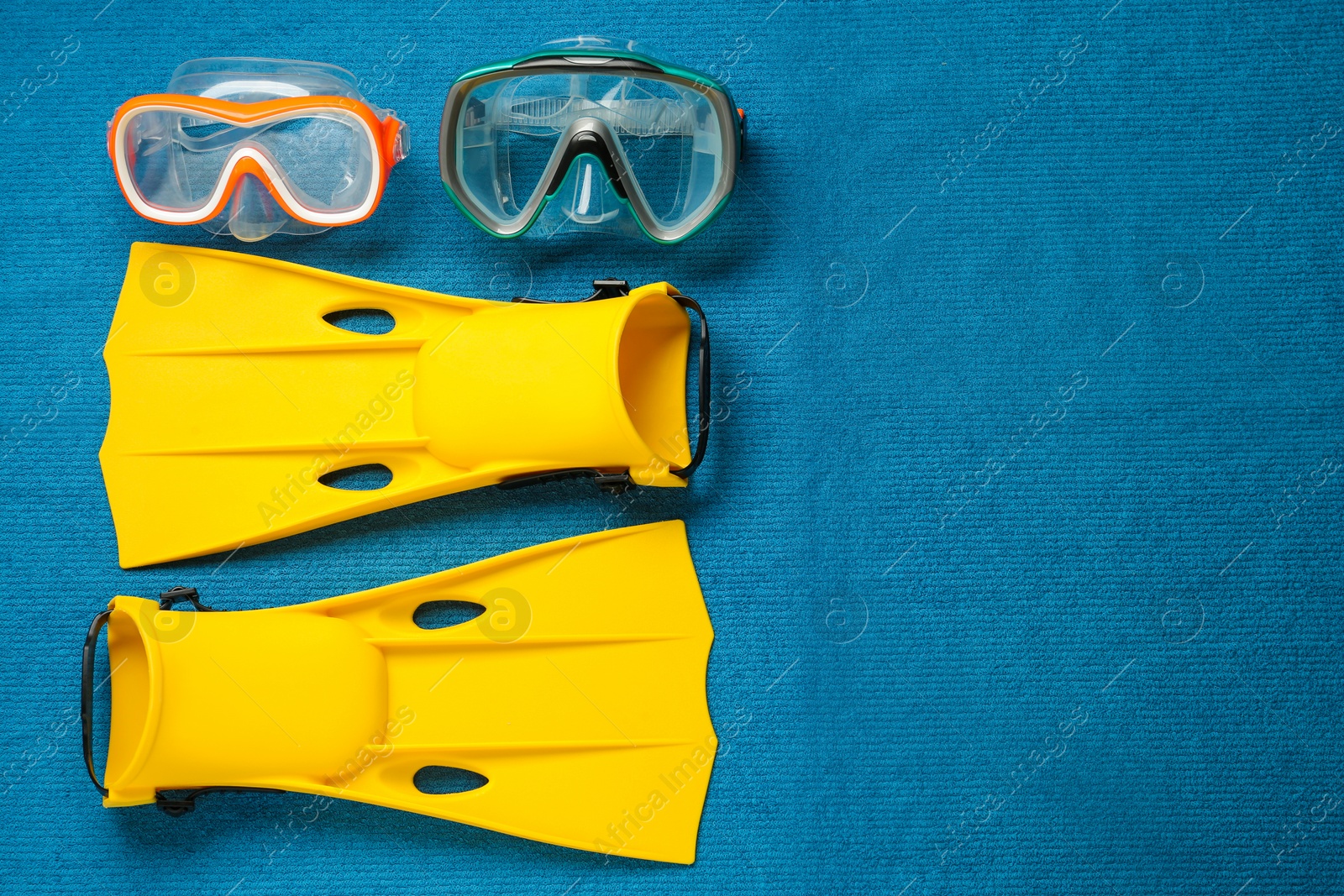 Photo of Pair of yellow flippers and masks on blue fabric, flat lay. Space for text